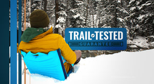 Trail Tested Guarantee - Person sitting in deep snow in an inflatable and insulating chair in front of a cold river