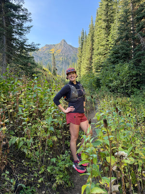 A woman wearing a running vest hiking in the forest and mountains