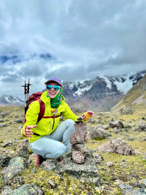 Woman smiling on top of a mountain with stacked rocks in front of her