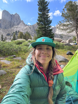 Woman smiling sitting at camp in front of giant sawtooth mountains