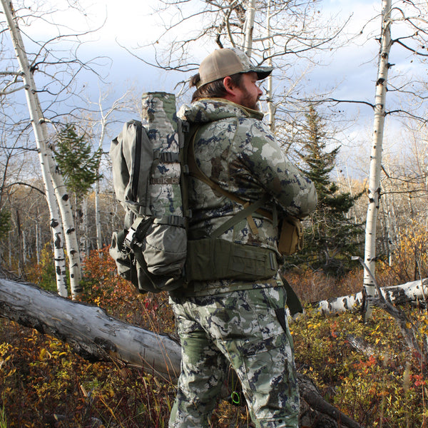 Man wearing a backpack with the crazy creek rolled up and attached to the side of it.
