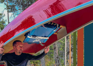 A man is portaging a canoe with a crazy creek paddle chair attached to the seat securely