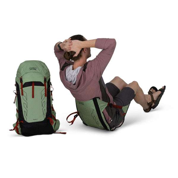 Backpacking man sitting - facing away in the Osprey and Crazy Creek Collab Hex chairon white - with backpack sitting next to him