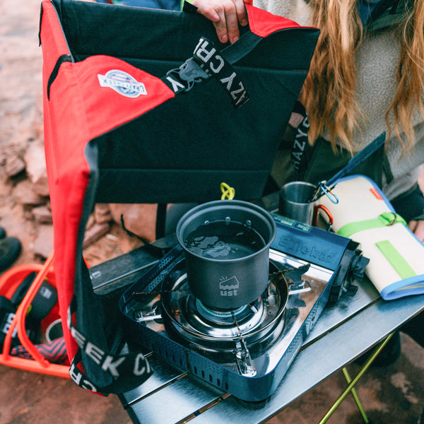 Person using a Crazy Creek chair as a windscreen for their portable camp stove