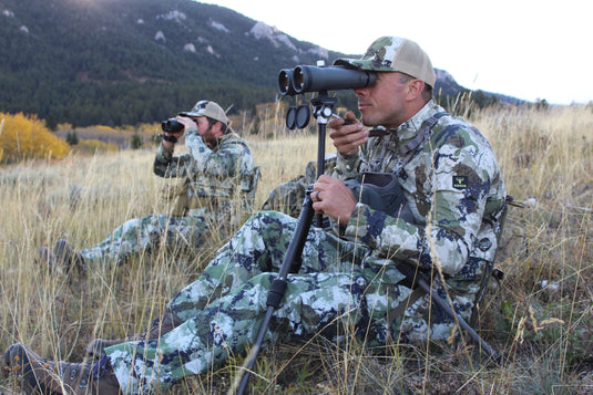 man using binoculars in camo crazy creek hex chair