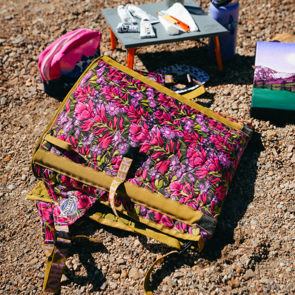 Floral-patterned Crazy Creek camping chair on a gravel surface with a small table in the background.