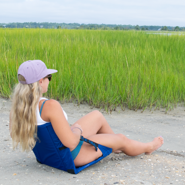 Woman sitting in blue crazy creek chair on a beach by green reeds